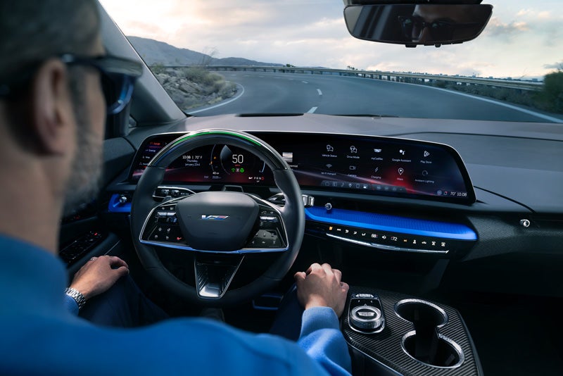 Front View of the 2026 OPTIQ-V Driving Through the Dusk Utilizing its Headlights | Serra Cadillac in Washington MI